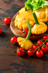 organic yellow patissons with cherry tomatoes and salad on a wooden table. a new harvest of vegetables from the garden, vegan food, a diet food. selective focus and copy space