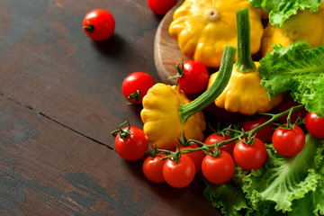 organic yellow patissons with cherry tomatoes and salad on a wooden table. a new harvest of vegetables from the garden, vegan food, a diet food. selective focus and copy space