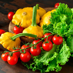 organic yellow patissons with cherry tomatoes and salad on a wooden table. a new harvest of vegetables from the garden, vegan food, a diet food. selective focus and copy space