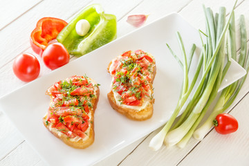 Bruschetta with fresh tomatoes and cheese on white boards next to fresh vegetables