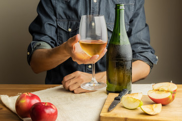 Beautiful ice cold glass and bottle of apple wine, with ripe apples in background. Male hands...