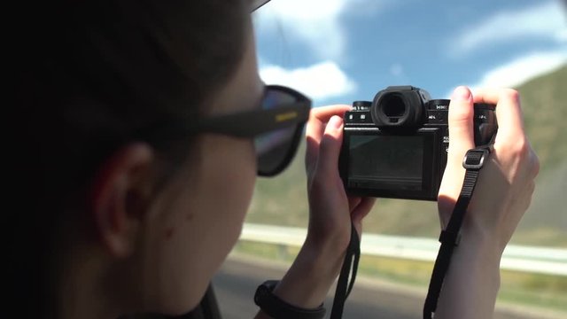beautiful asian girl in black sunglasses taking photos of mountains with vintage camera on road trip in convertible car.