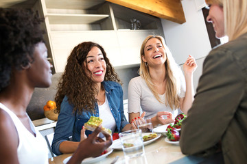 Group of friends laughing while eating healthy food at home.
