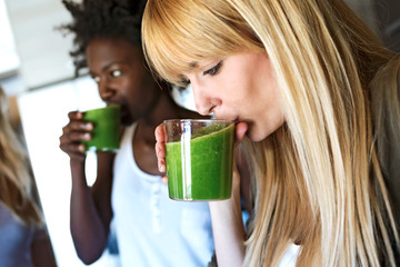 Beautiful young women drinking detox green juice at home.