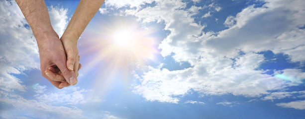 Soulmates Hand in Hand - mature male and female hands holding against a beautiful summery blue sky with sun burst background and plenty of copy space
