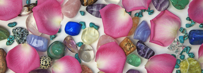 Petals and crystals holistic banner - wide background with random tumbled stones and pink petals on...