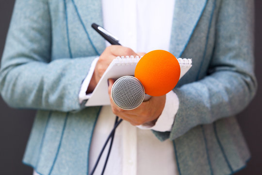Female reporter at press conference, writing notes, holding microphone