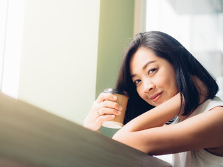 Asian woman drinks hot coffee in the cafe with warm light.