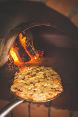 Close up image of a freshly baked gourmet wood fired pizza as it gets taken out of the pizza oven