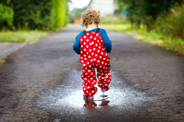 Close-up of little toddler girl wearing rain boots and trousers and walking during sleet, rain on...