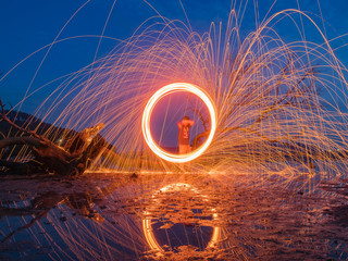 light lines of steel wool with long exposure, speed motion abstract background in the dark night with dry branch tree and reflection in water