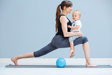 young sporty mother does physical yoga or pilates exercises together with her toddler baby son over...
