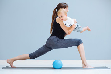young sporty mother does physical yoga or pilates exercises together with her toddler baby son over...