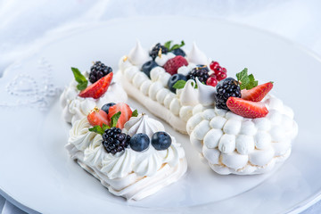 Delicate white meringues with fresh berries on the plate on white background. Dessert Pavlova close-up. Wedding cake.