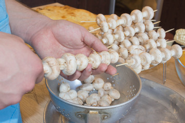 Preparing shashlik for barbecue grill. A man hand puts pieces of mushrooms on skewer