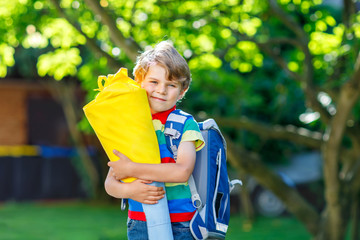 little kid boy with school satchel on first day to school, holding school cone with gifts