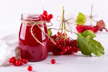 Glass jar of homemade viburnum jam with fresh berries  on white table.