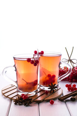 Hot spicy beverage with viburnum in glass cups  with fresh viburnum berries and cinnamon sticks, anise stars on a white kitchen table.