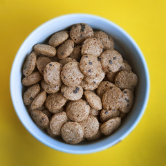Crunchy granola isoalted. Nourishing muesli with chocolate in white round bowl over yellow background. Daily breakfast. Square Image.