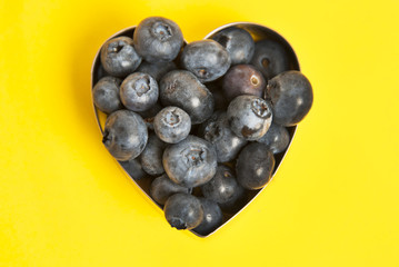 Blueberry heart shape symbol concept for healthy eating and lifestyle. Isolated on yellow background.