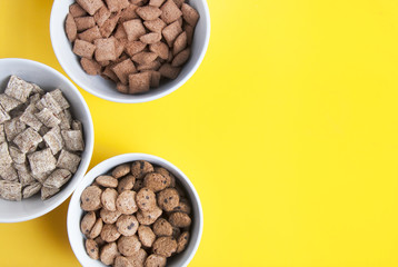Bowls of whole grain muesli, granola and oat meals with copy space. Isolated on yellow background. Top view. Daily breakfast food.