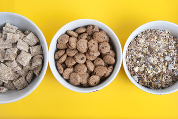 Bowls of whole grain muesli, granola and oat meals with copy space. Isolated on yellow background. Top view. Daily breakfast food.