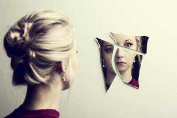 Woman looking at her face in three shards of broken mirror