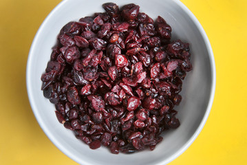 Dried fruits or berries, sweet cranberries isolated on yellow background in round white bowl. Ingredients for healthy breakfast. Top view.