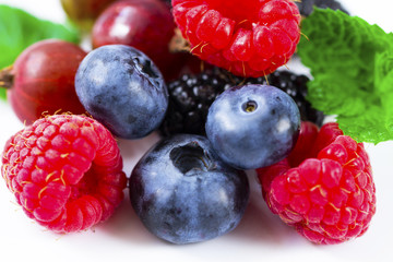 Close-up arrangement mixed, assorted berries including blackberries, strawberry, blueberry, raspberries and fresh leaf on white