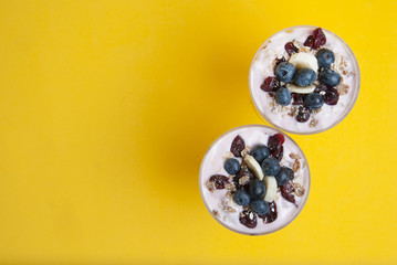 Obraz na płótnie Canvas Breakfast in glass cup. Granola oat meals, with dried fruits, blueberries and yogurt. Health breakfast or sweet dessert. Isoalted on yellow background. Copy space.