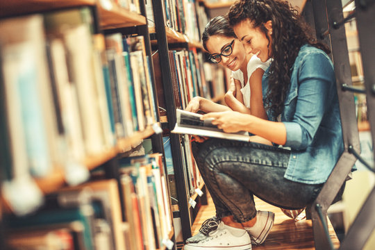 Two female students read and learns by the book shelf at the city library.Reading a book.