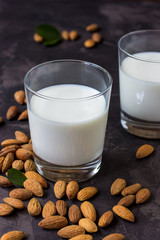 Almond milk in glass and almonds nuts on a dark background
