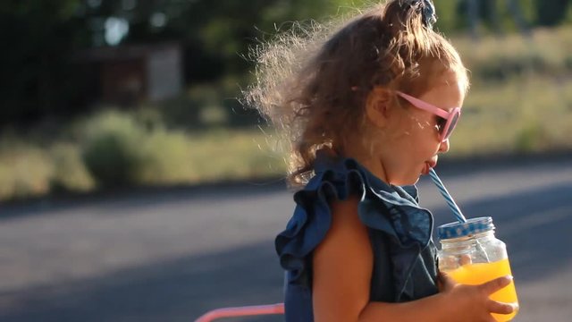 Child girl in sunglasses drinks smoothies in the rays of sunset on a summer day. Close up