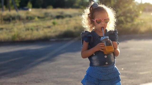 Child girl in sunglasses drinks smoothies in the rays of sunset on a summer day.