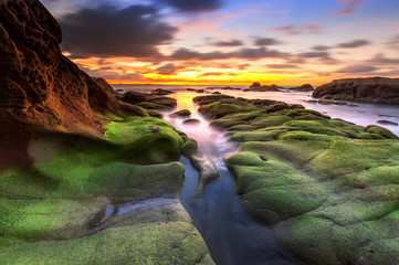 view of beautiful sunset sky at unknown beach in Sabah, Malaysia. Natural coastal rocks covered by...