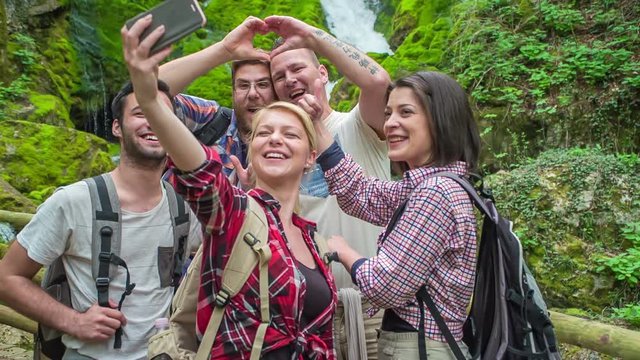 Friends are taking a photo of themselves in front of a waterfall. The day is really beautiful.