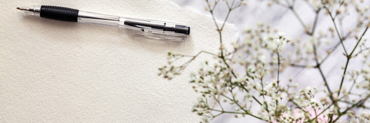 Handmade paper, black pen and white small flowers on a marble table