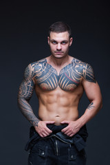 Fototapeta na wymiar The man with a muscular naked torso with tattoos on the dark background. ABS