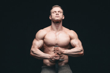 Bodybuilder man posing with a sword isolated on black background. Serious shirtless man...