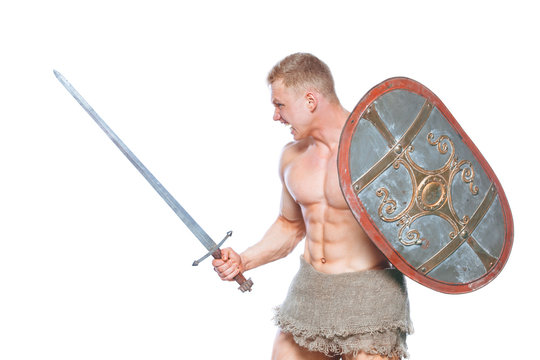 Bodybuilder man posing with a sword and shield isolated on white background. Serious shirtless man demonstrating his mascular body.