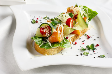 Bruschetta with salmon red fish, fresh vegetables and herbs on a white plate