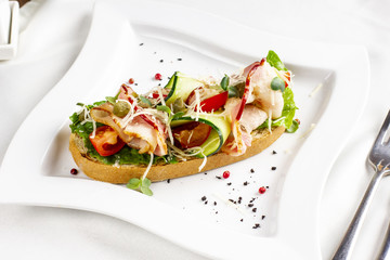Bruschetta with bacon, fresh vegetables and capers on white plate
