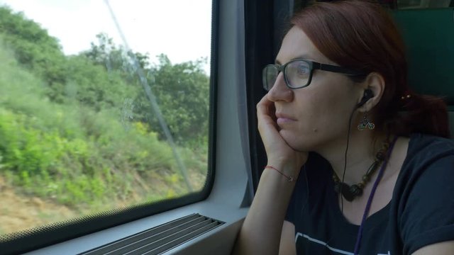 Girl with eyeglasses and earphones looking through train window while travelling.