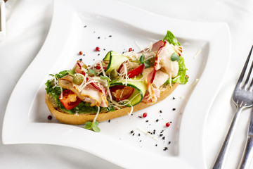 Bruschetta with bacon, fresh vegetables and capers on white plate