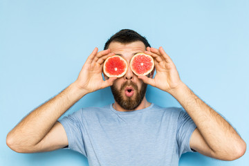 Young man holding slices of grapefruit in front of his eyes