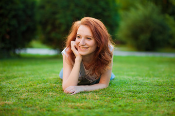 Naklejka na ściany i meble Red-haired girl lying on the lawn in the Park