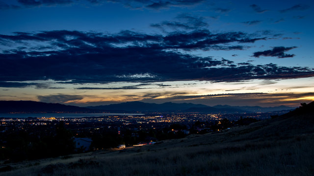 Dusk falls over a sleepy city in a valley with mountains and a lake in the background