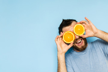 Young man holding slices of orange in front of his eyes