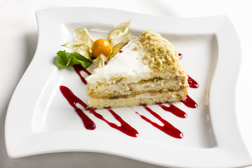 The piece of cake with cream and physalis on white plate