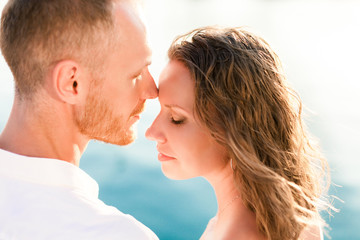 Couple of travelers are sitting by blue sea during romantic honeymoon vacation at sunset after wedding. Man and woman are happy tourists in resort. Lovers are wearing in white clothes outdoor.